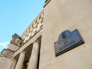 Stone government building facade with tall columns, seated statues and a plaque reading Ministry of Defence.
